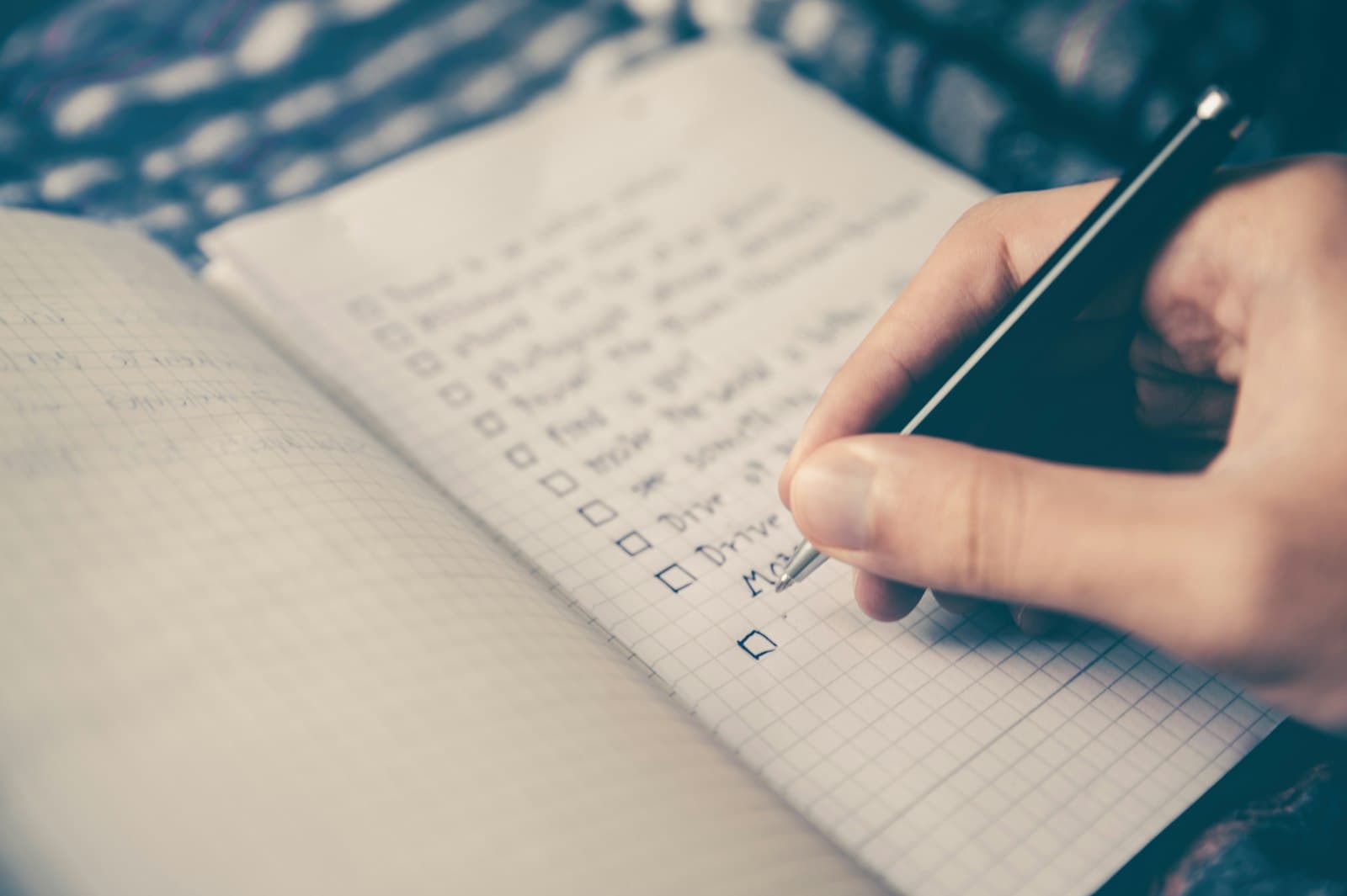 Main cochant une liste écrite au stylo dans un carnet quadrillé